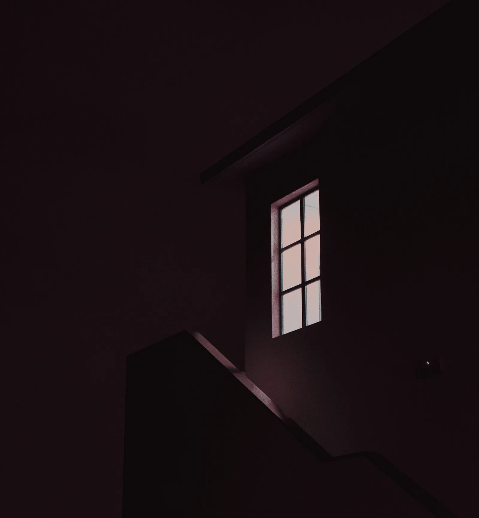 Uma única janela acesa na parede de uma casa, à noite
