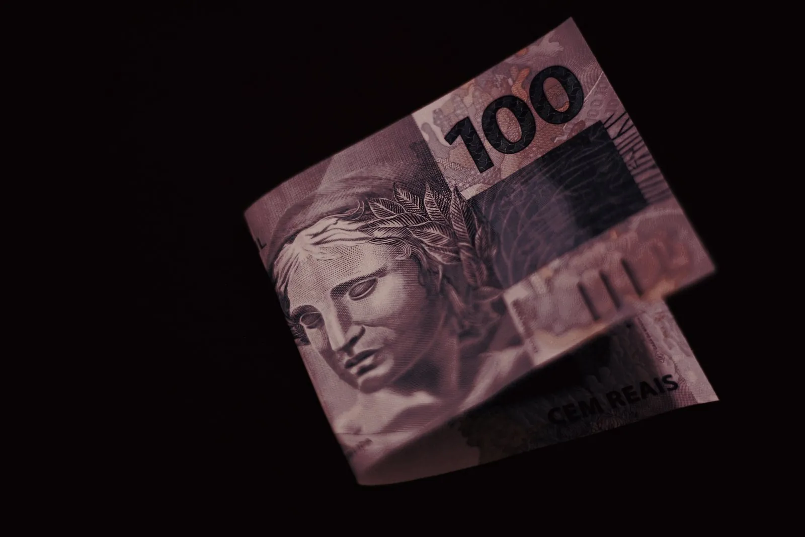 Nota de cem reais dobrada sobre fundo preto